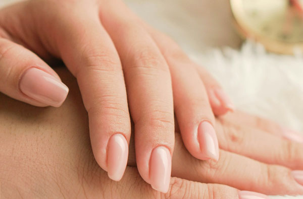 Pink manicured hands holding a clock. Pedi tools visible in the background.