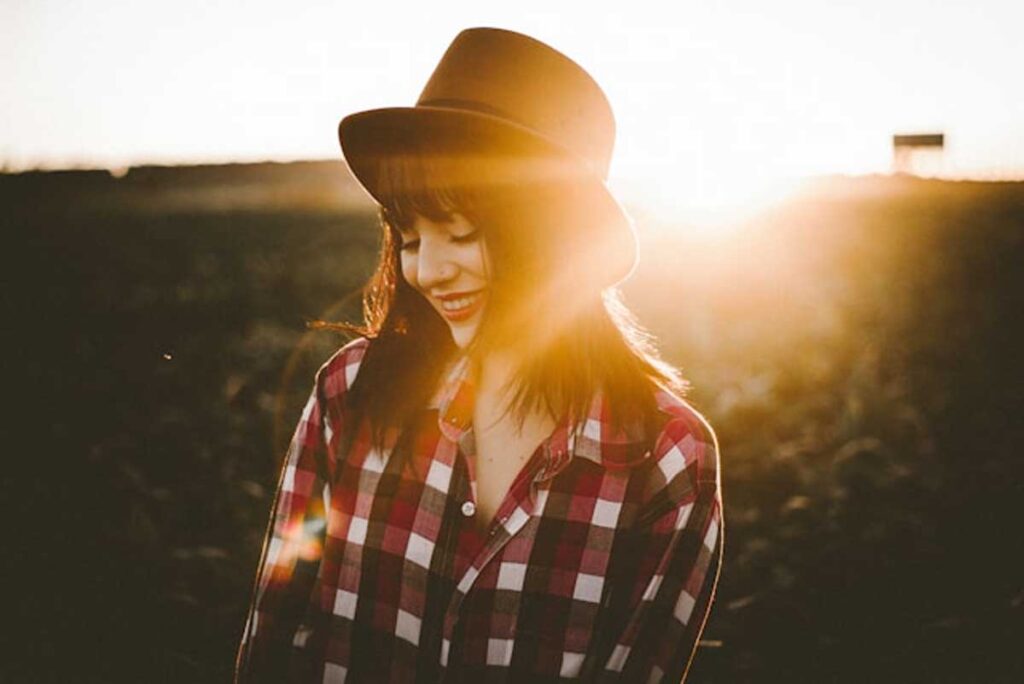 A woman in a hat and plaid shirt standing in a field of wildflowers.